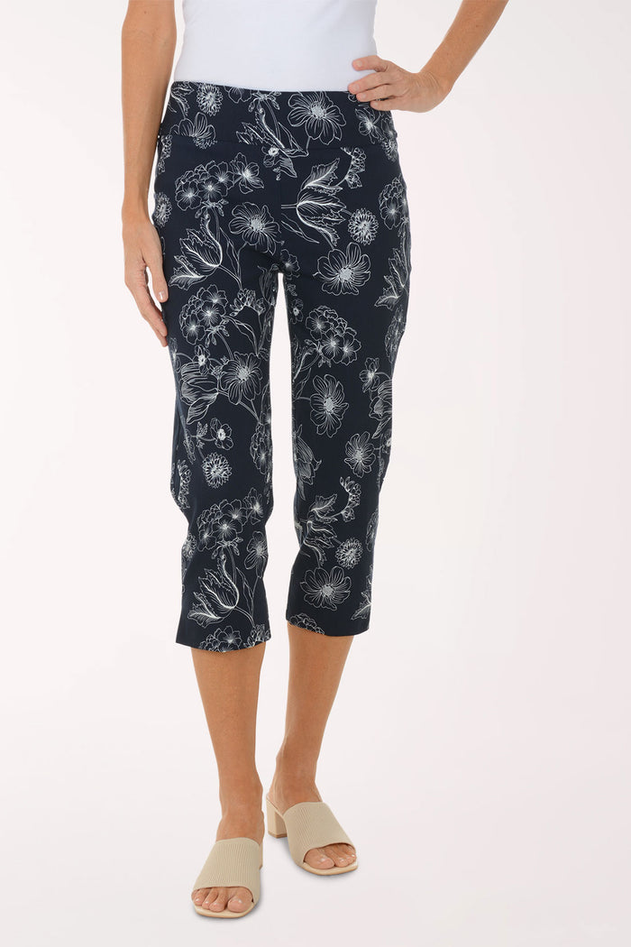 Person wearing navy capri pants with white floral pattern on a white background