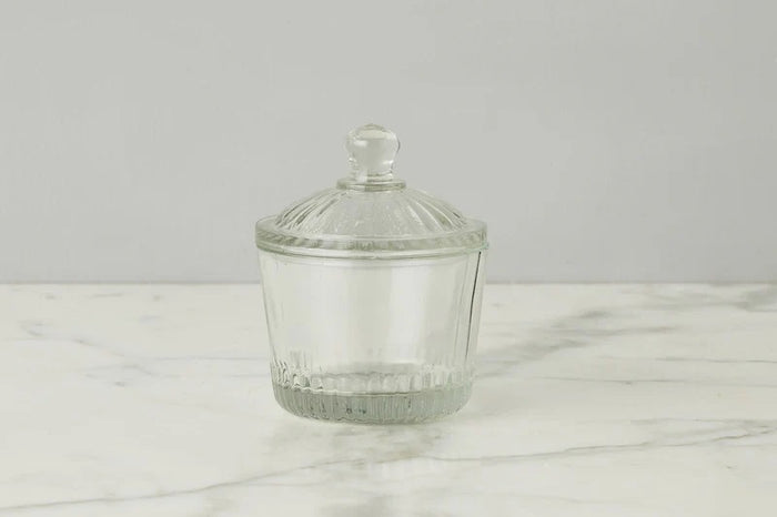 Two ETUHOME Bistro Glass Bon Bon Jars with ribbed lids sit on a wooden surface, one filled with yellow candies and the other nearly empty. Wrapped sweets are scattered nearby, creating a charming ETUHOME display.