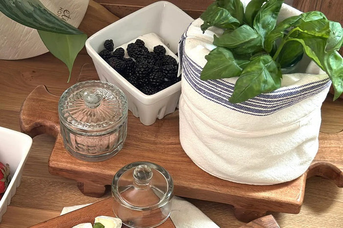 The ETUHOME Bistro Glass Salt Cellar with Scoop sits on a wooden tray atop a marble counter, accompanied by two other glass jars for herbs and sugar. A small wooden scoop from ETUHOME rests in front.