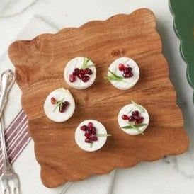 Three small savory tarts, paired with green leaves, are displayed on the ETUHOME Natural Square Scalloped Cheese Board with Markers, set against a floral-patterned background.