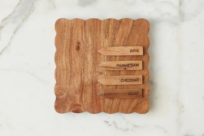 Three small savory tarts, paired with green leaves, are displayed on the ETUHOME Natural Square Scalloped Cheese Board with Markers, set against a floral-patterned background.