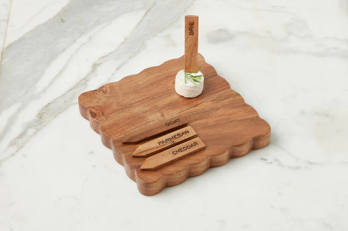 Three small savory tarts, paired with green leaves, are displayed on the ETUHOME Natural Square Scalloped Cheese Board with Markers, set against a floral-patterned background.
