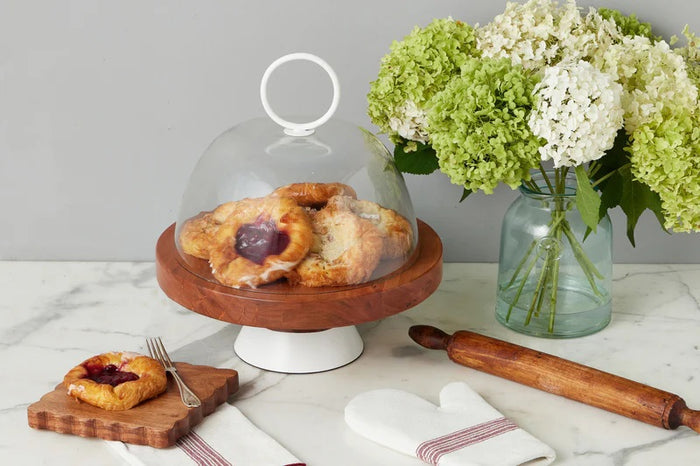 Three small savory tarts, paired with green leaves, are displayed on the ETUHOME Natural Square Scalloped Cheese Board with Markers, set against a floral-patterned background.