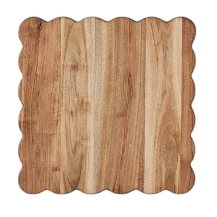 The ETUHOME Natural Square Scalloped Cutting Board, Medium, crafted from durable acacia wood, stands upright against a light gray wall on a white marble surface.