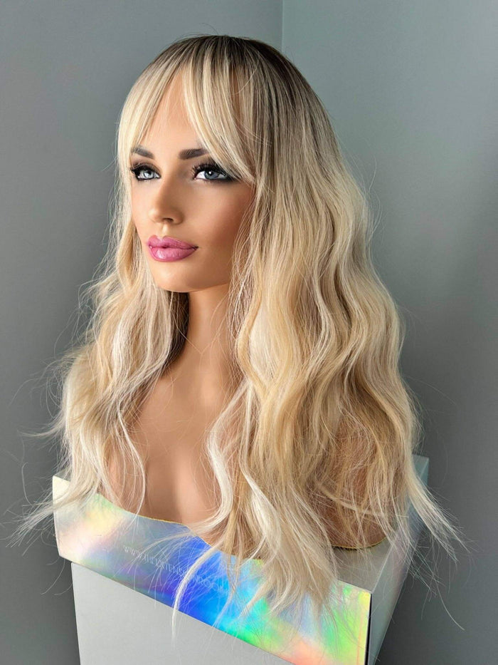 Blonde wig with wavy hair styled on a mannequin head against a gray background