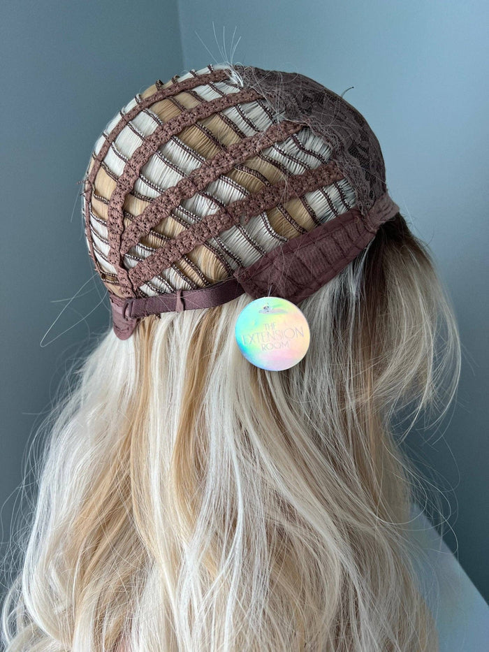 Brown knit cap with a colorful pom-pom on a person with blonde hair against a gray background