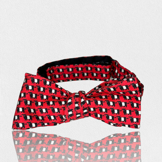 The COLLARED GREENS FEARRINGTON SIGNATURE COLLECTION - BESPOKE BELTIE BOW TIE IN RED features a black and white geometric pattern on silk, handmade neckwear displayed on a white textured surface.