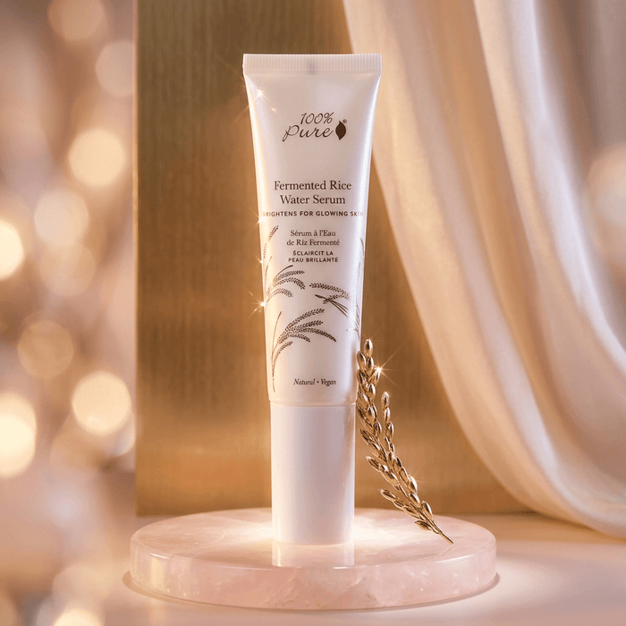 Tube of 100% Pure Fermented Rice Water Serum on a decorative stand with a soft, blurred background.