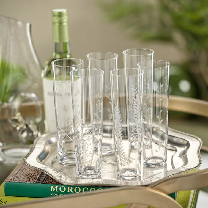 Six FLORA ETCHED CHAMPAGNE FLUTES by ZODAX are lined up in a row. Each clear glass showcases a unique, subtle etched botanical or leaf pattern, beautifully contrasting against a white background.