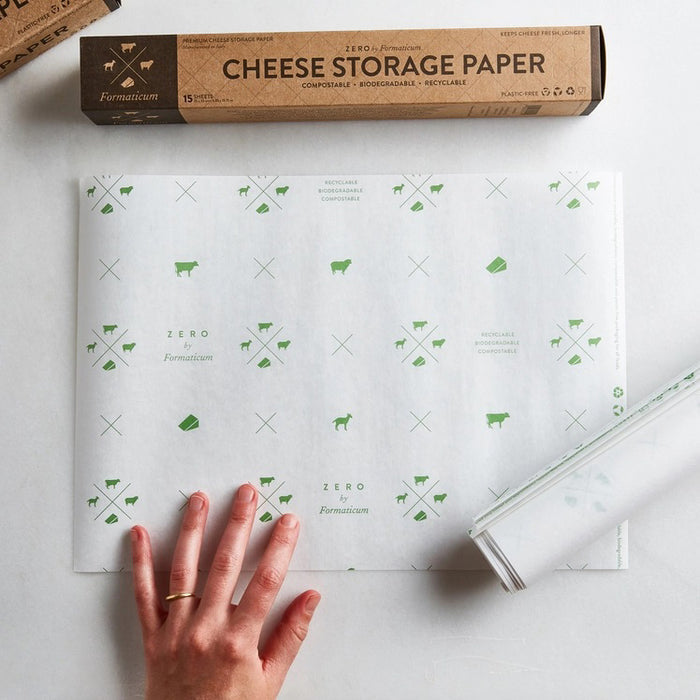 A hand holds a sheet of FORMATICUM - ZERO CHEESE STORAGE PAPER with green illustrations, next to a brown FORMATICUM box. The partially unrolled cheese storage paper is ideal for keeping cheese fresh at home.