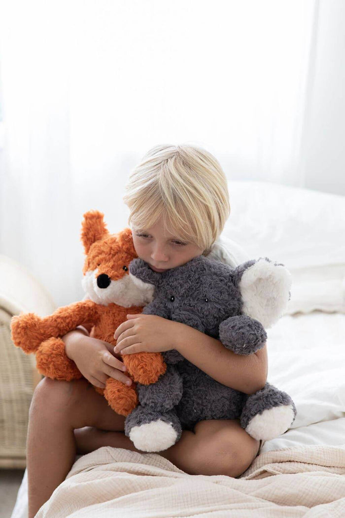 Child hugging Frankl The Weighted Fox teddy and a gray plush elephant on a cozy bed.
