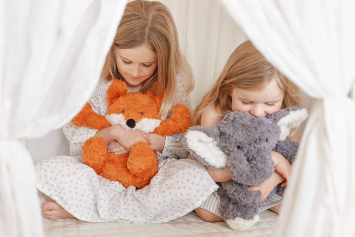 Two children cuddling Frankl The Weighted Fox teddy and an elephant plush toy in a cozy setting.