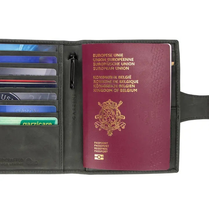The GARZINI RFID-blocking leather passport holder in black features an AirTag compartment and snap button closure, shown on a white background.