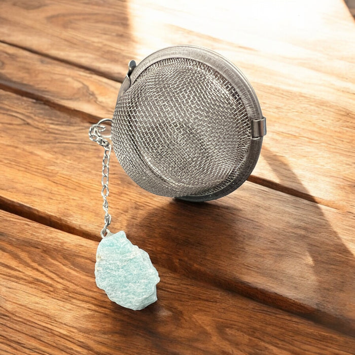 Metallic tea ball infuser with a chain on a wooden surface, Raven's Cauldron, 6 N Sandusky St, Delaware, OH 43015