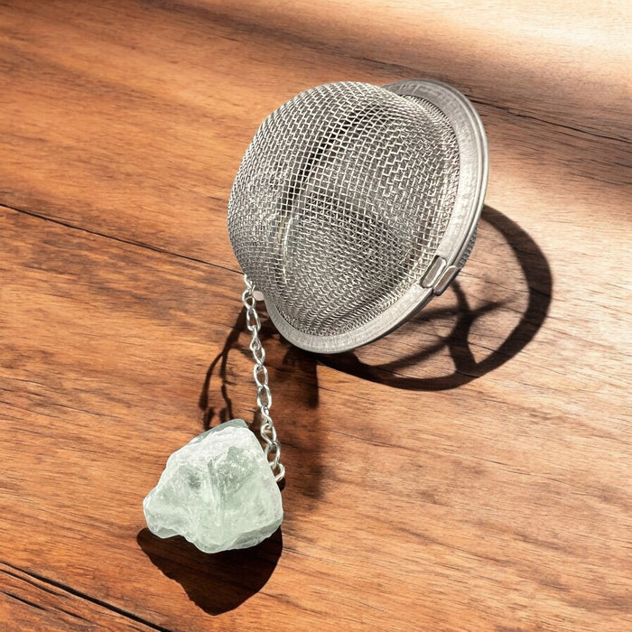 Metallic tea ball infuser with a chain on a wooden surface, Raven's Cauldron, 6 N Sandusky St, Delaware, OH 43015