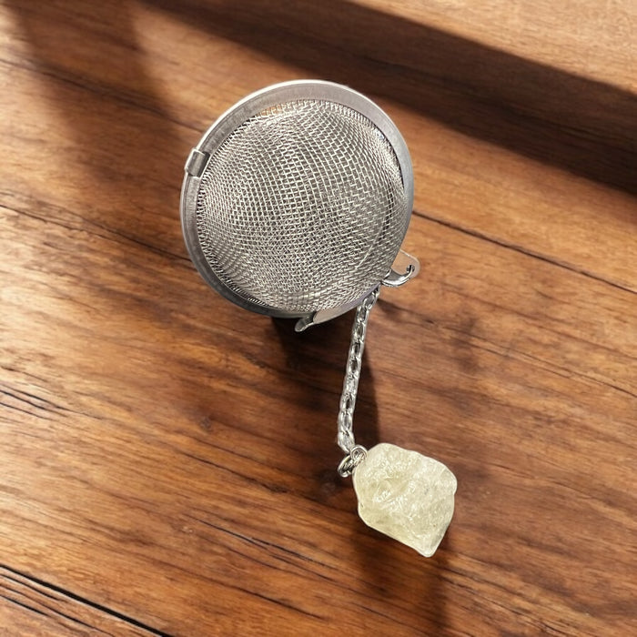 Metallic tea ball infuser with a chain on a wooden surface, Raven's Cauldron, 6 N Sandusky St, Delaware, OH 43015