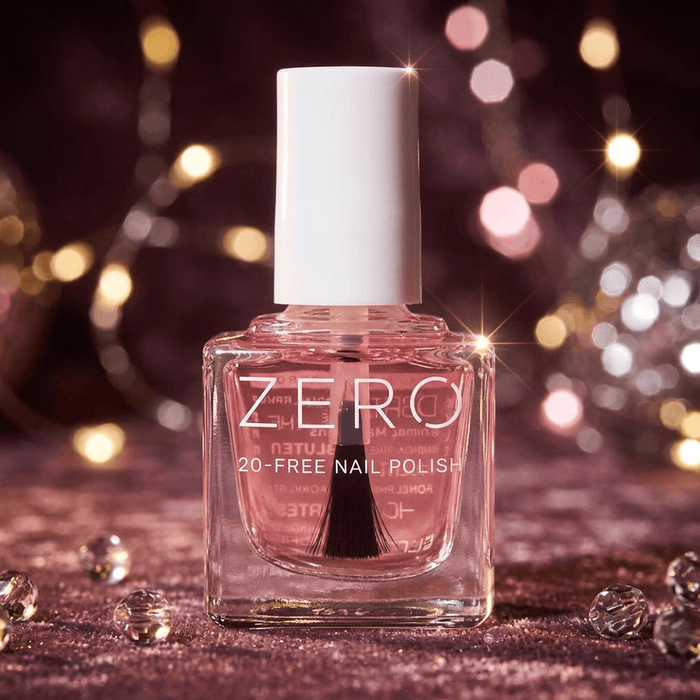 Pink nail polish bottle with white cap on a glittery surface with blurred lights in the background