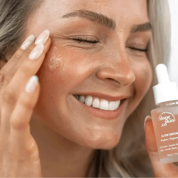 Woman applying Glow Serum on her face, showcasing radiant skin and a happy smile.