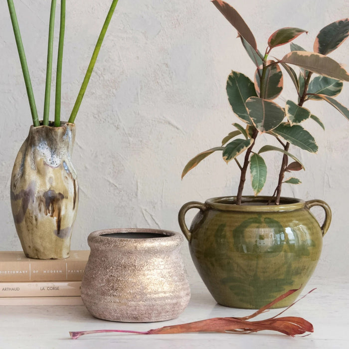 The GREEN HAND-PAINTED TERRACOTTA URN WITH HANDLES by CREATIVE COOP is a round, green ceramic vase with two handles and a glossy finish, featuring hand-painted leaf and floral designs for artisan charm.