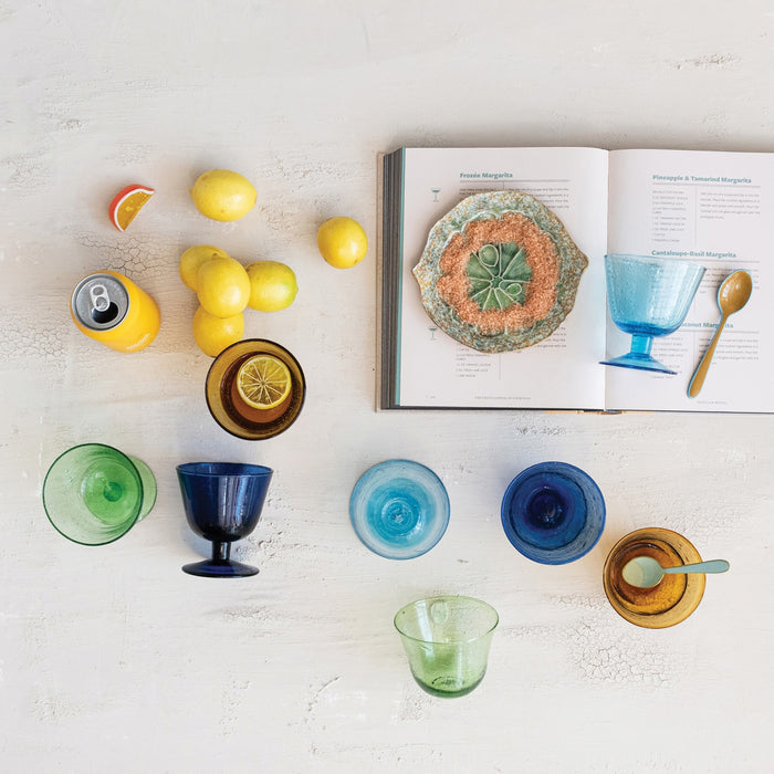 The HAND-BLOWN STEMMED SEEDED GLASS by CREATIVE COOP is a green-tinted goblet with a wide bowl, short stem, and round base. Its hand-blown seeded glass features visible bubbles and a gradient with richer green at the bottom.