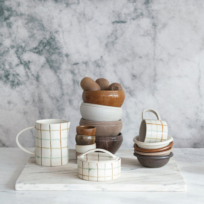 Close-up of the HAND-PAINTED STONEWARE PITCHER by CREATIVE COOP, showcasing an artisanal beige surface with a grid of brown, orange, and light green, plus small dark speckles for added charm.