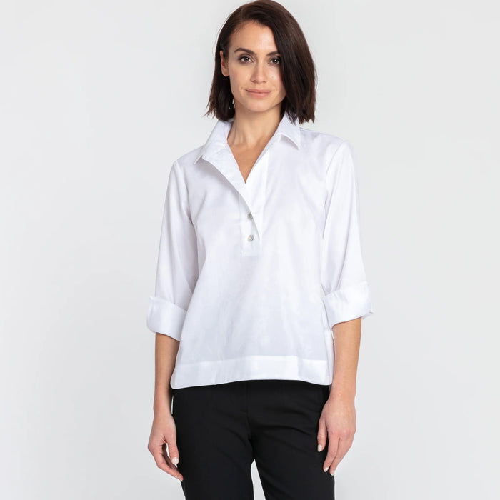 A woman with short dark hair models the HINSON WU - AILEEN 3/4 SLEEVE POLISHED COTTON SHIRT in navy, featuring a collared neckline, stretch fabric, and three buttons. She pairs it with white pants and poses against a plain light gray background.