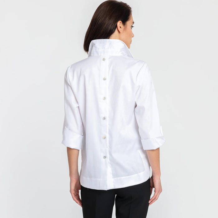 A woman with short dark hair models the HINSON WU - AILEEN 3/4 SLEEVE POLISHED COTTON SHIRT in navy, featuring a collared neckline, stretch fabric, and three buttons. She pairs it with white pants and poses against a plain light gray background.