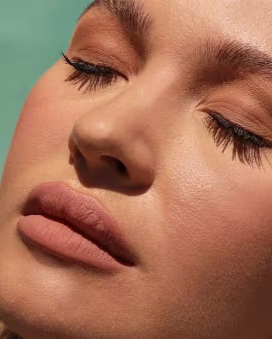 A round container of JASON WU BEAUTY READY SET MATTE 1 - TRANSLUCENT BANANA setting powder with a black lid and beige powder rests on a light brown textured surface.