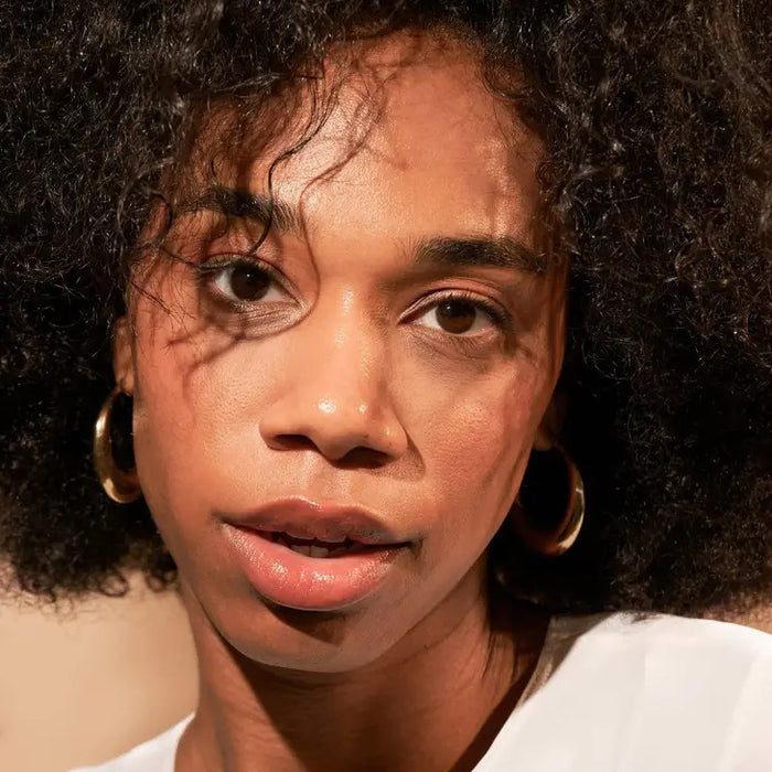 A black tube labeled "JW" stands before a beige swatch, highlighting JASON WU BEAUTY's TINTED MOISTURIZER MEETS CC CREAM for a natural glow on a white background.