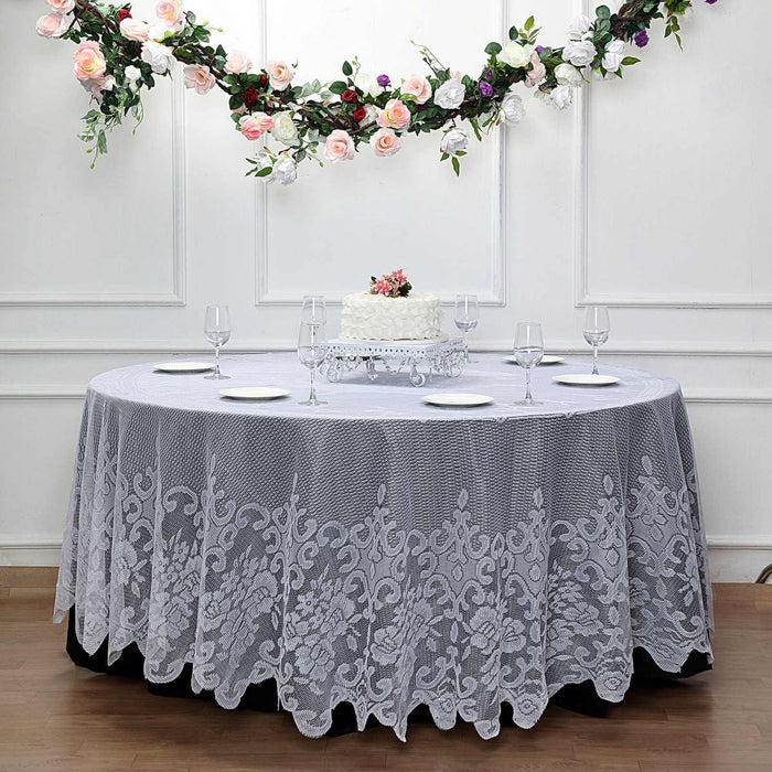 Elegant lace tablecloth draped over a round table with floral decor and cake.