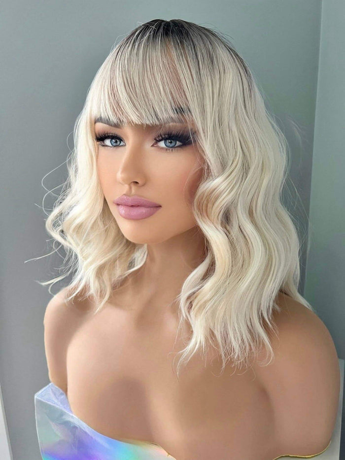 Lilah Short White Blonde Body Wave Wig with Bangs featuring soft waves and light bangs framing the face.