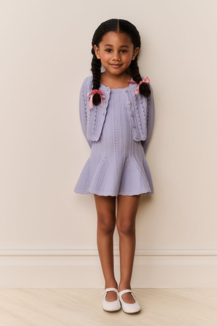 Young girl wearing a light blue cardigan and dress outfit against a plain background