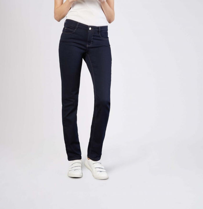 Model wears MAC - DREAM STRAIGHT LEG DENIM by MAC in light blue with a white shirt and white sneakers, standing with one hand in their pocket against a plain light gray background.