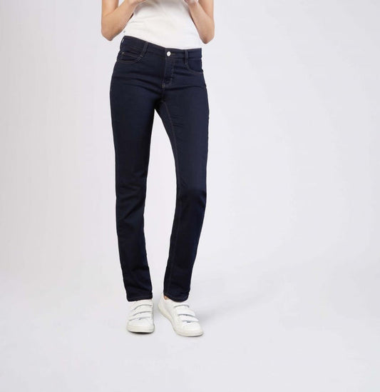 Model wears MAC - DREAM STRAIGHT LEG DENIM by MAC in light blue with a white shirt and white sneakers, standing with one hand in their pocket against a plain light gray background.