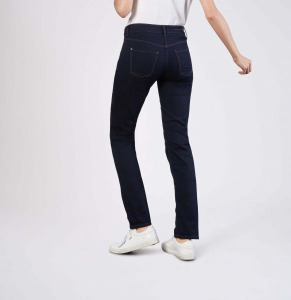 Model wears MAC - DREAM STRAIGHT LEG DENIM by MAC in light blue with a white shirt and white sneakers, standing with one hand in their pocket against a plain light gray background.