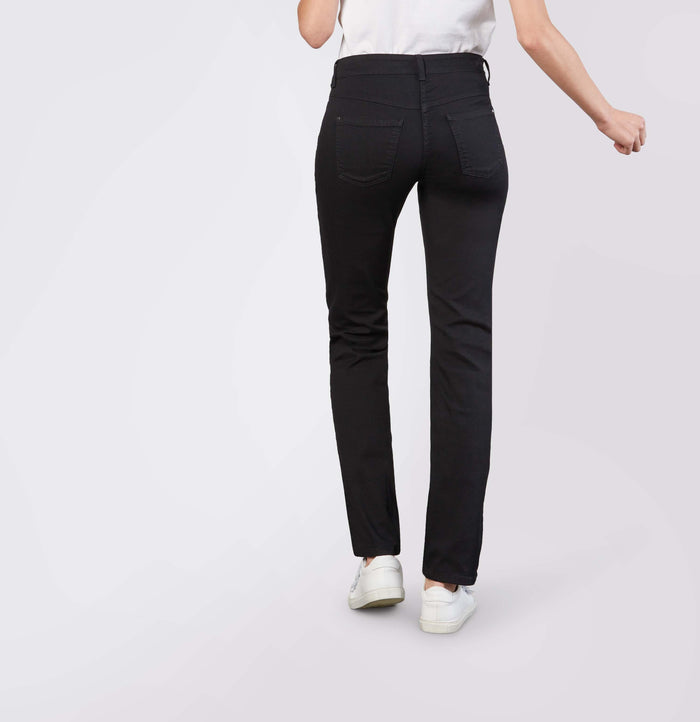 Model wears MAC - DREAM STRAIGHT LEG DENIM by MAC in light blue with a white shirt and white sneakers, standing with one hand in their pocket against a plain light gray background.