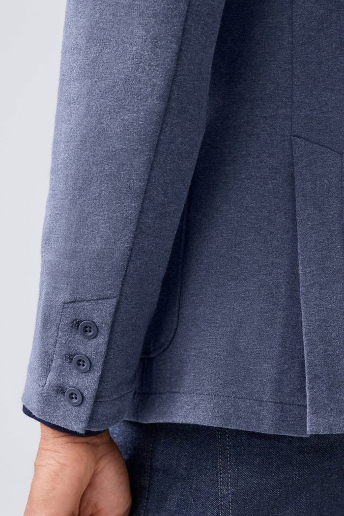 A person in a navy shirt holds open the MACK WELDON ACE BLAZER IN TRUE BLACK, revealing its comfortable, machine-washable design with an inside pocket and inner lining.