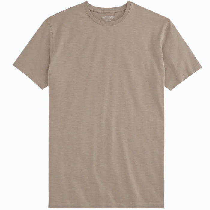 A man with short dark hair and a beard wears the Mack Weldon Silver Crew Neck T-Shirt in Desert Taupe, paired with dark jeans and a wristwatch. He stands against a light gray background, looking slightly to the side with a neutral expression.