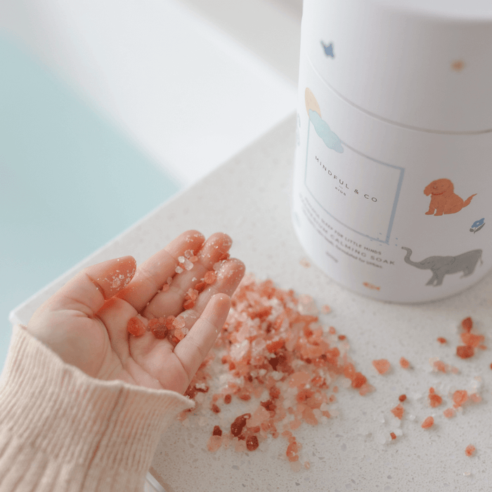 Magnesium Calming Soak 600g in a hand with pink bath salts spilled on a white counter.