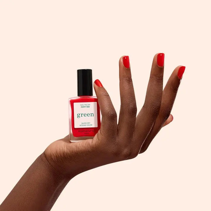 A bottle of MANUCURIST INC’s GREEN™ Nail Polish in Poppy Red, featuring a vibrant red liquid, a black cap, and a label displaying the word “green” prominently.