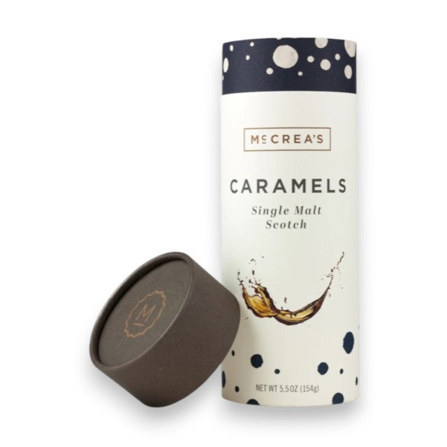 A cylindrical container with a dark lid sits next to it, both adorned with McCrea's Candies branding. The container is labeled "MCCREA'S CANDIES - SINGLE MALT SCOTCH CARAMELS" and features an image of caramel flowing like a liquid. These rich-flavored caramels promise indulgence without the worry of a hangover. The net weight is 5.5 oz (154g).