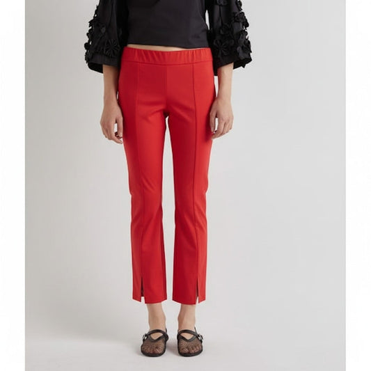 A person wearing MEIMEIJ - Cotton Front Hem Slit Pant in Coral, paired with a black top featuring textured floral sleeves and black flat shoes, stands against a plain white background.