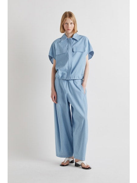 Model wears MEIMEIJ - DRAWSTRING COTTON PANTS in light blue, featuring a loose fit, wide legs, cropped ankle, and drawstring waist. Styled with white sandals. Image shows shoulders to feet against a plain background.