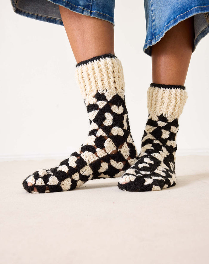 Introducing the MERSEA - LA PAZ CROCHET SLIPPER SOCKS by MERSEA: These hand-crocheted slipper socks feature a striking black and cream geometric design. The toes, heels, and cuffs are crafted in a solid cream shade, while the body showcases alternating black and cream sections—resulting in cozy socks you'll love to slip on.