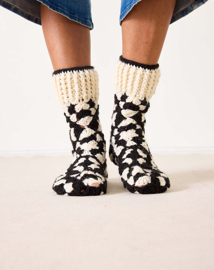 Introducing the MERSEA - LA PAZ CROCHET SLIPPER SOCKS by MERSEA: These hand-crocheted slipper socks feature a striking black and cream geometric design. The toes, heels, and cuffs are crafted in a solid cream shade, while the body showcases alternating black and cream sections—resulting in cozy socks you'll love to slip on.