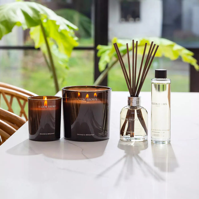 A dark brown MOLTON BROWN ORANGE AND BERGAMOT LUXURY CANDLE 3 WICK releases a refreshing citrus and neroli scent, displayed against a plain light background.