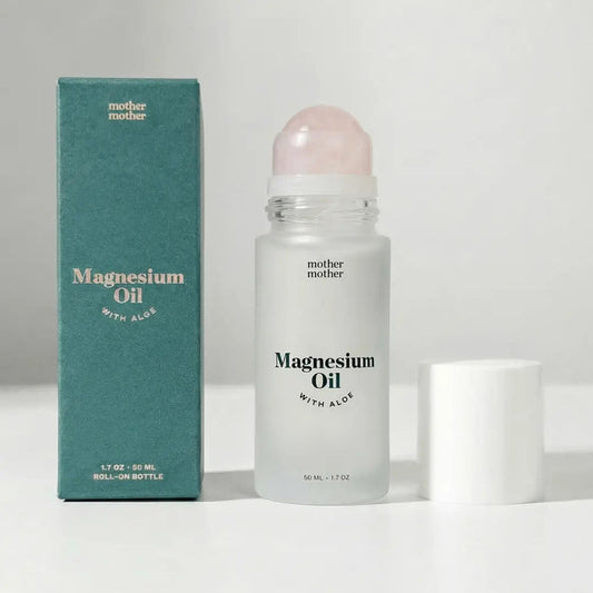 A green box and a frosted roll-on bottle of MOTHER MOTHER - MAGNESIUM OIL & ALOE ROLLER are displayed side by side. Designed for sensitive skin, the bottle from MOTHER MOTHER has its white cap removed and set to the right on a white surface.