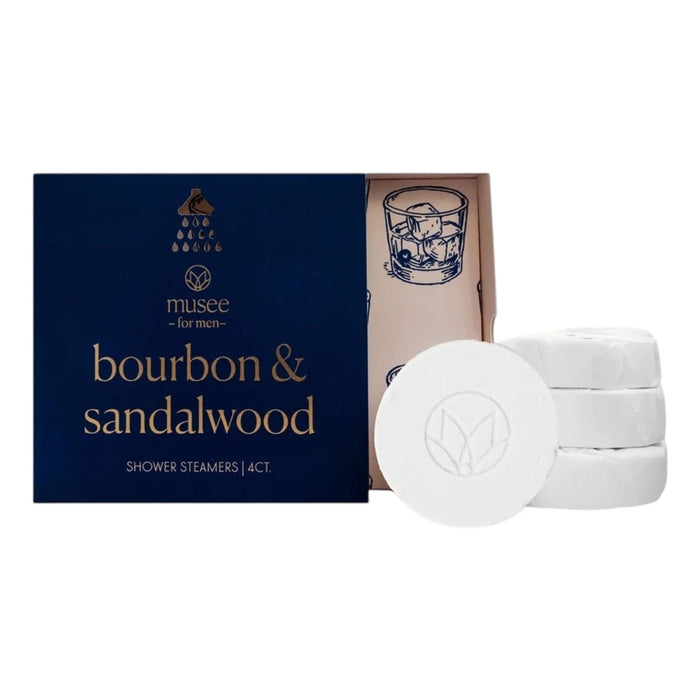 A blue box labeled “MUSEE - BOURBON & SANDALWOOD SHOWER STEAMERS” by MUSEE sits beside four white round steamers and an open lid adorned with a drawing of a whiskey glass, offering an indulgent aromatherapy shower experience enhanced with sandalwood essential oil.