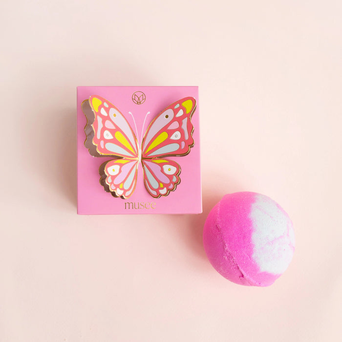 The MUSEE - BUTTERFLY BOXED BATH BALM by MUSEE, a handcrafted pink and white bath balm, sits beside its matching pink box adorned with a vibrant butterfly illustration and the “musee” logo at the bottom. Made with natural ingredients, this luxurious bath product promises a soothing and indulgent experience.