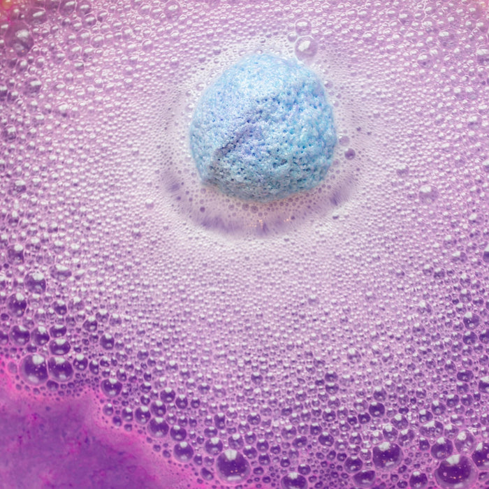 Instructional graphic with text on how to use the MUSEE - DREAMWEAVER THERAPY BATH BALM by MUSEE, featuring a dissolving colorful bath balm in pink bubbly water within a white flower outline on a pink background.